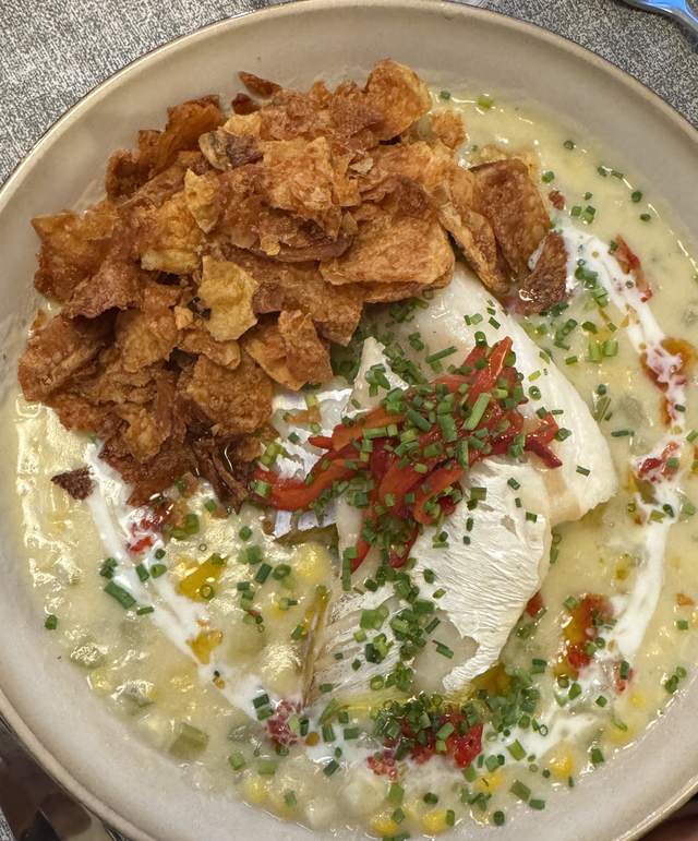 A fillet of cod in a shallow bowl of sweet corn chowder, under
                chives, strips of roasted red Fresno chili and a pile of crushed
                kettle chips.