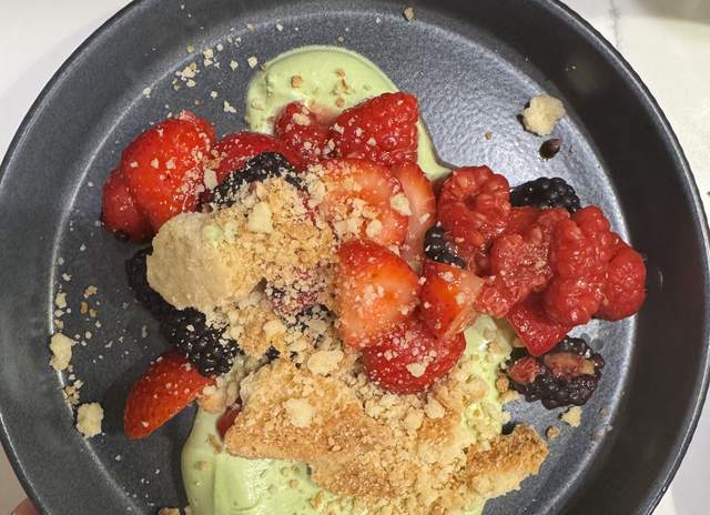 Strawberries, raspberries and blackberries piled on pale green
                matcha mascarpone cream in a dark stoneware bowl, scattered with
                shortbread crumble.