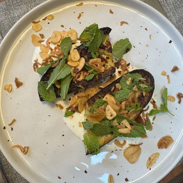 Two blackened halves of zucchini on a wide cream plate, over lemon
                garlic yogurt, covered in garlic chips, crisp shallots and mint.