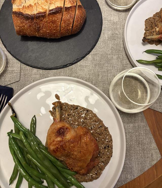 Crispy-skinned chicken thigh with au poivre sauce and lemony
                green beans, with sliced sourdough on a slate board nearby.