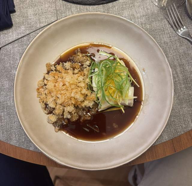 Steamed cod in a shallow bowl with ginger and scallion ribbons,
                surrounded by light soy sauce and pieces of crispy rice.