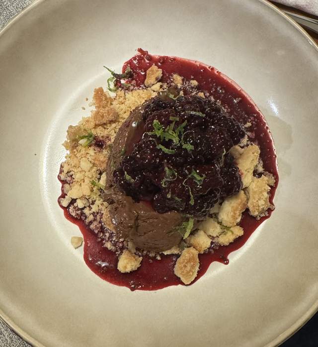 A scoop of dark chocolate mousse in a wide cream bowl, under
                blackberry compote and lime zest, ringed with shortbread crumbs
                and a pool of purple juice.